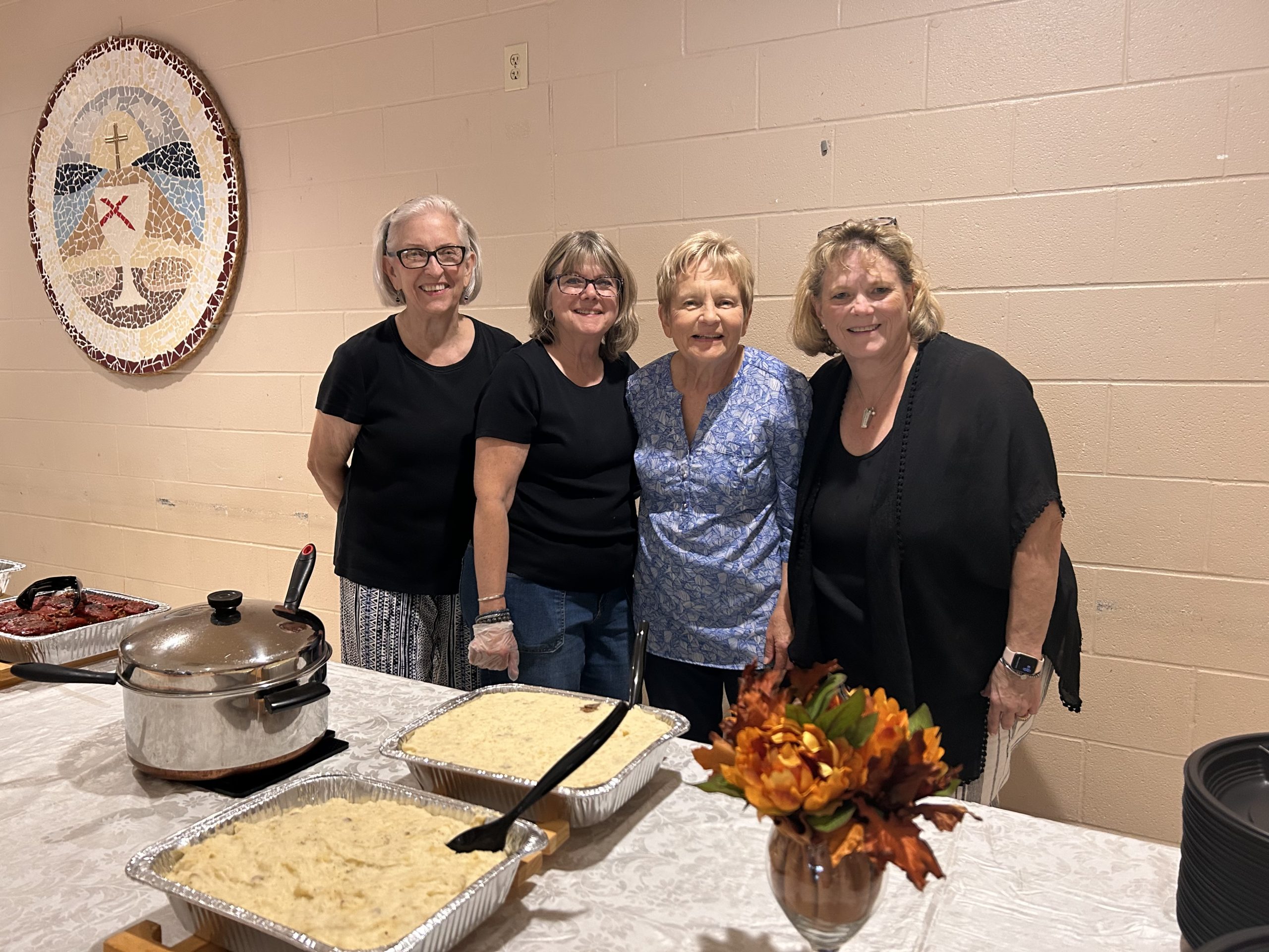 Four women smiling behind a buffet